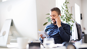 Man aan telefoon bij laptop